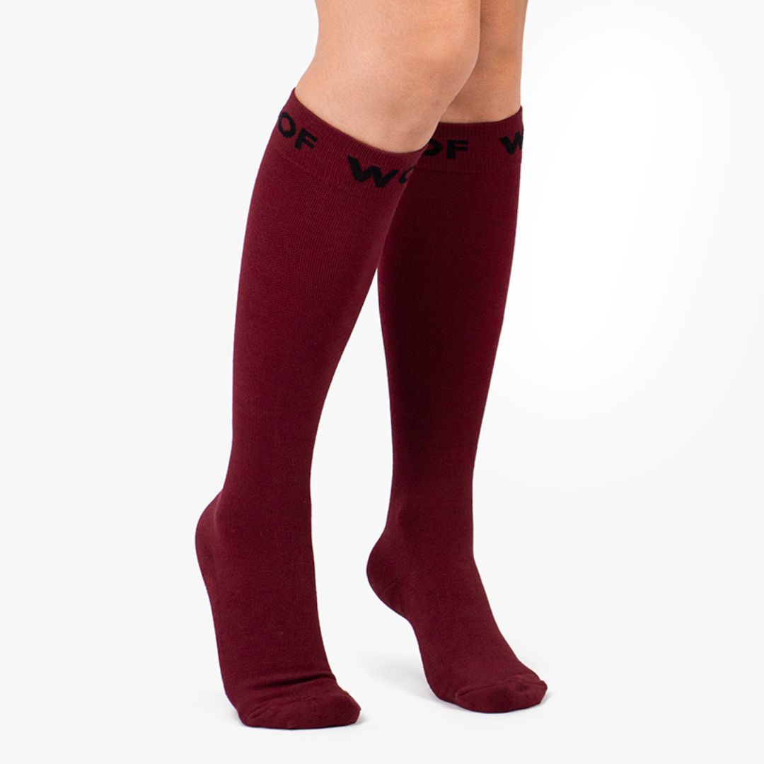 Nurse wearing solid maroon knee-high compression socks with black top cuff branding.
